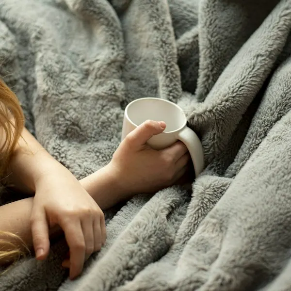 A woman wrapped in a gray knit throw holding a mug
