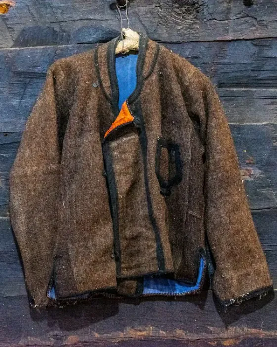 A brown wool jacket hanging on a weathered wooden wall
