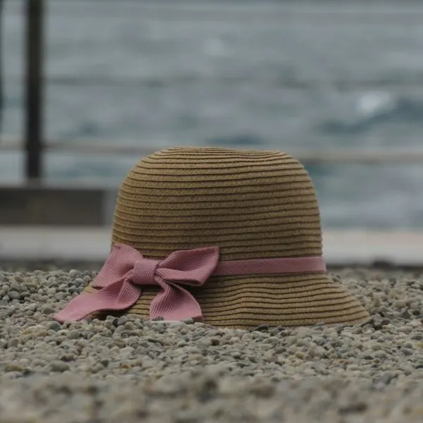 A straw hat with a pink bow on pebbles