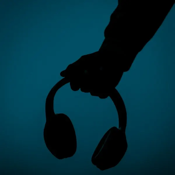 A hand holding over-ear headphones against a teal wall