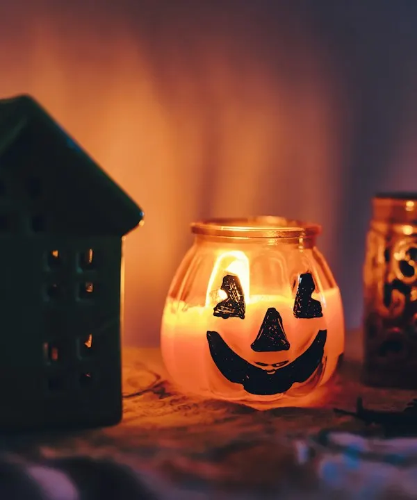 A ceramic jack-o'-lantern candle holder glowing beside a small ceramic house