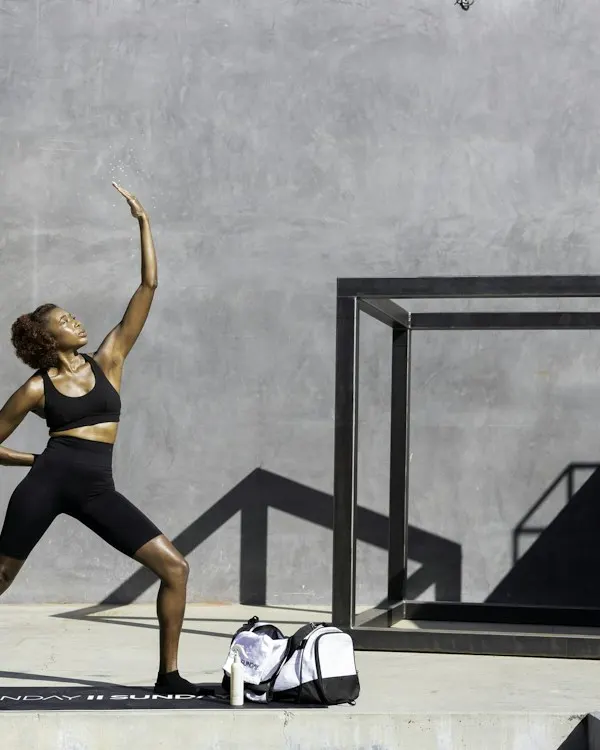 A runner in black tights and crop top stretching against a concrete wall