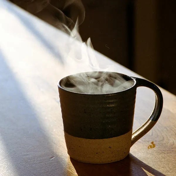 A steaming stoneware mug in morning sun