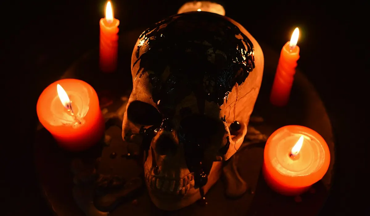 Lit candles around a dark ceramic skull on a black table