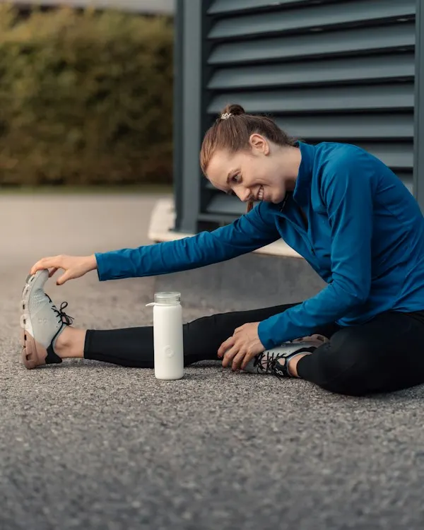 A woman in a blue half-zip stretching on the pavement