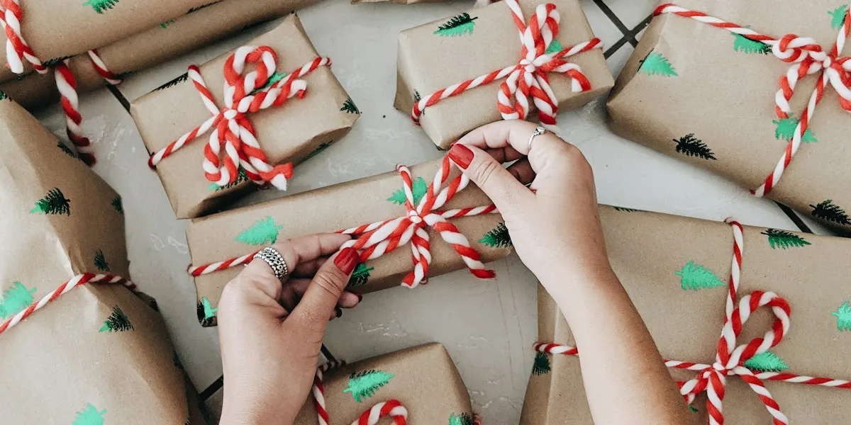 Hands wrapping presents in brown paper and red and white twine